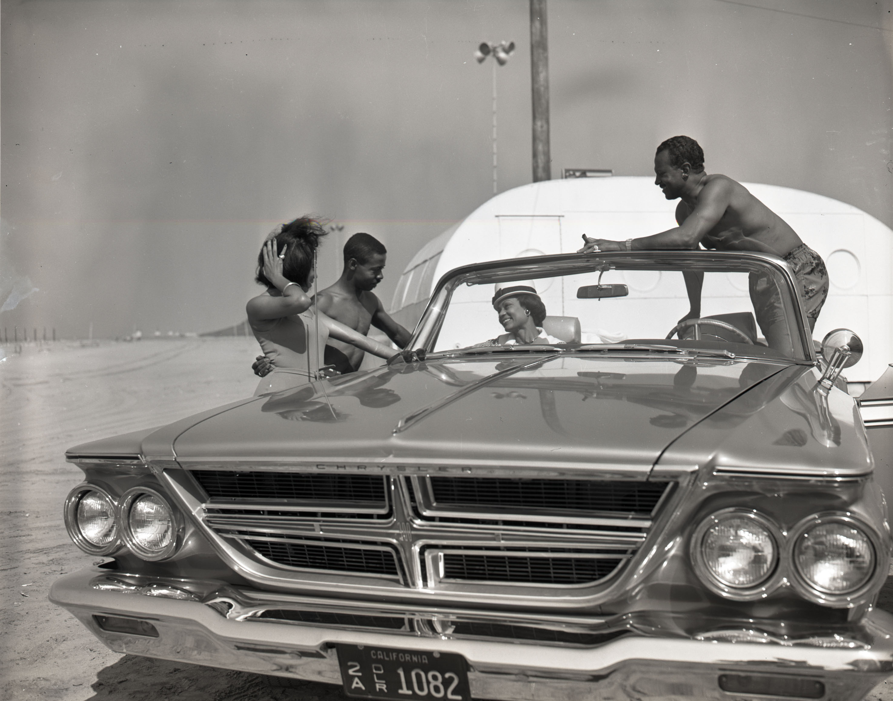 Man and woman in a convertible with the top down talking to a man and a woman next to the car