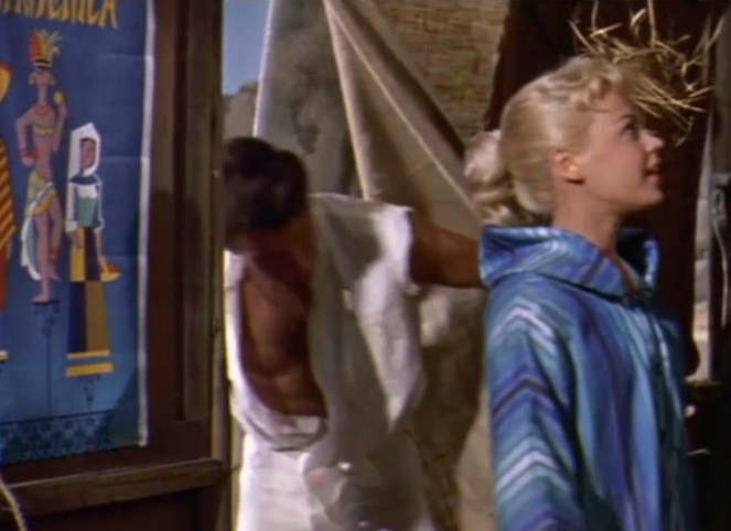 A young girl stares at inside of a beach hut while a man enters the hut in the background