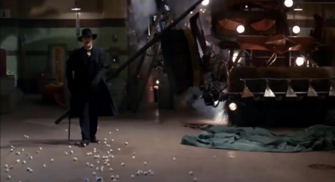Man in dark suit, hat, glasses, and cane stands amid a factory floor next to a machine containing acid.